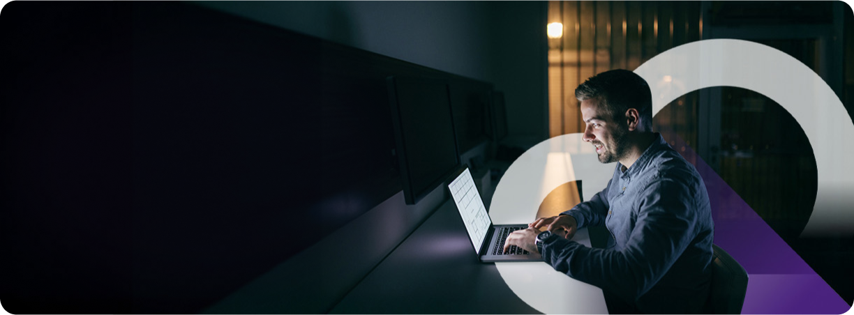 Man working on a laptop in a dimly lit room, surrounded by abstract geometric shapes.