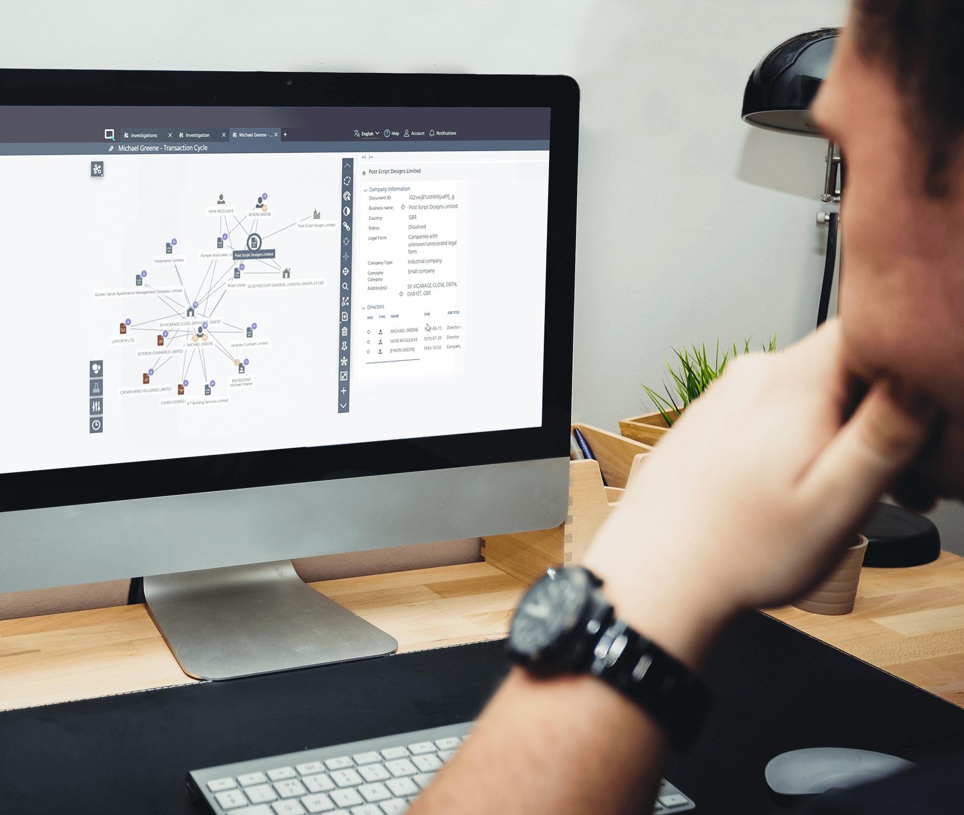 Person viewing a network diagram on a computer screen at a desk, with a keyboard, mouse, and small plant nearby.